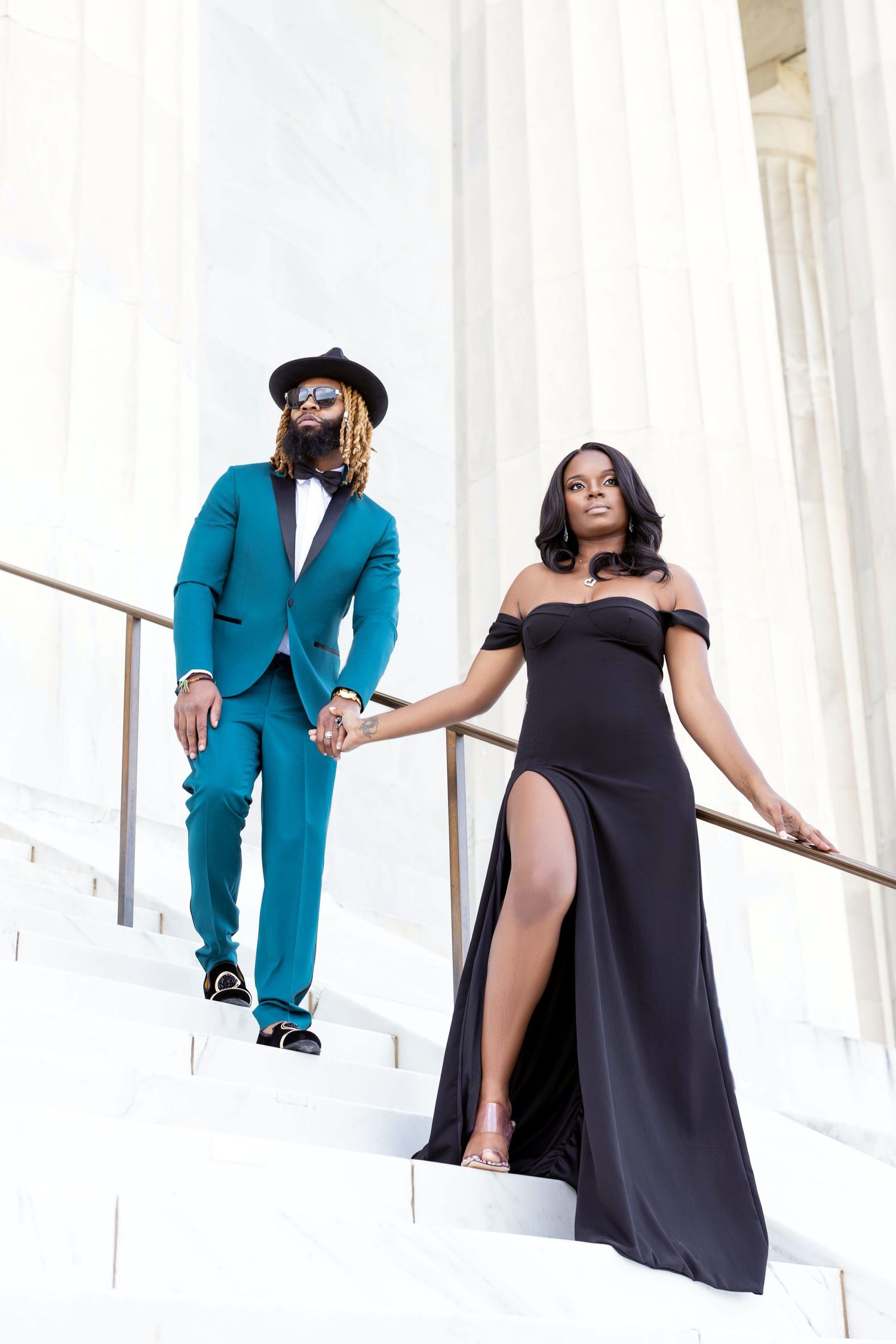 Dramatic stairway photo of a couple in formal wear against white columns.