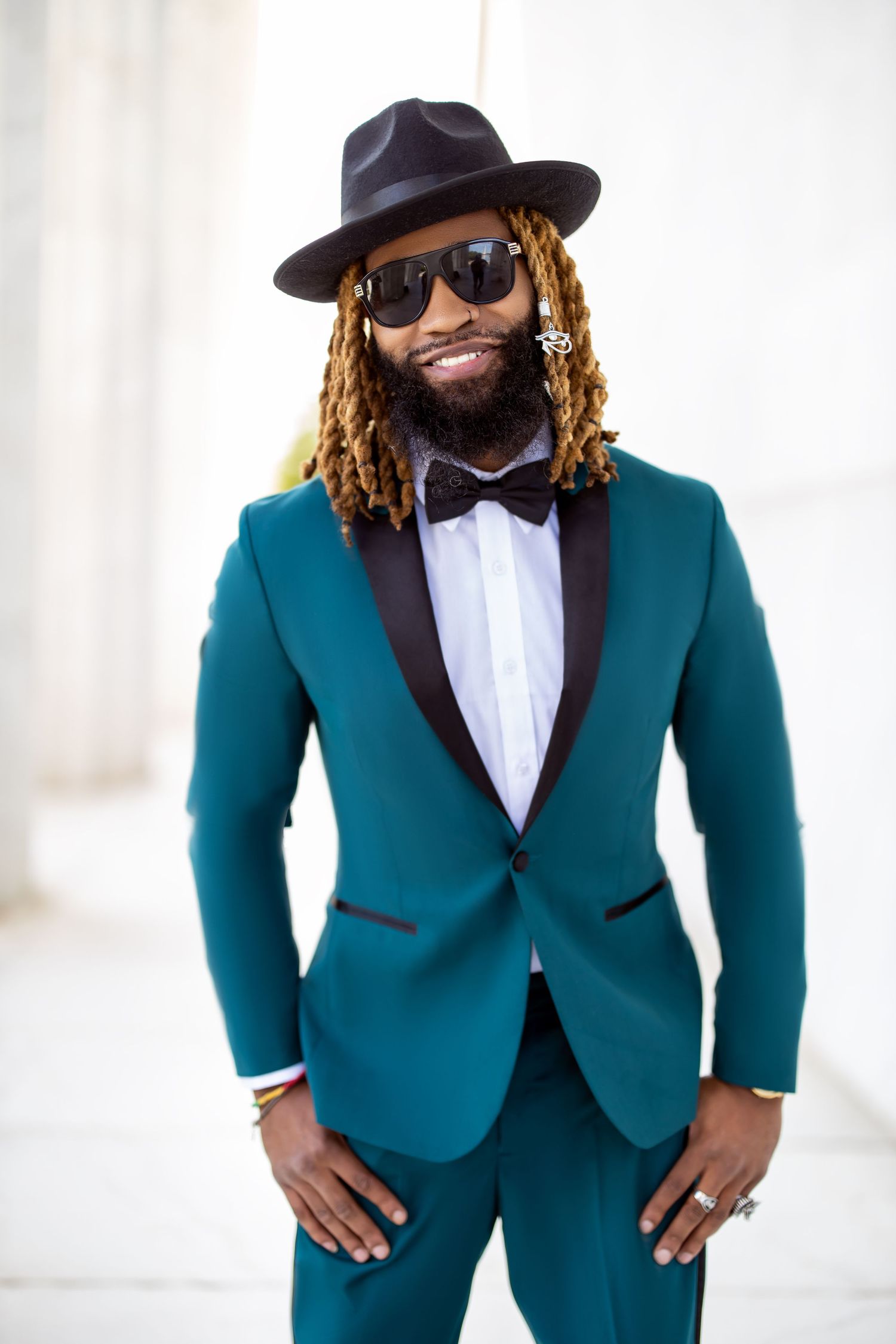 Stylish portrait of a man in teal suit, bow tie and fedora hat with blonde dreadlocks.