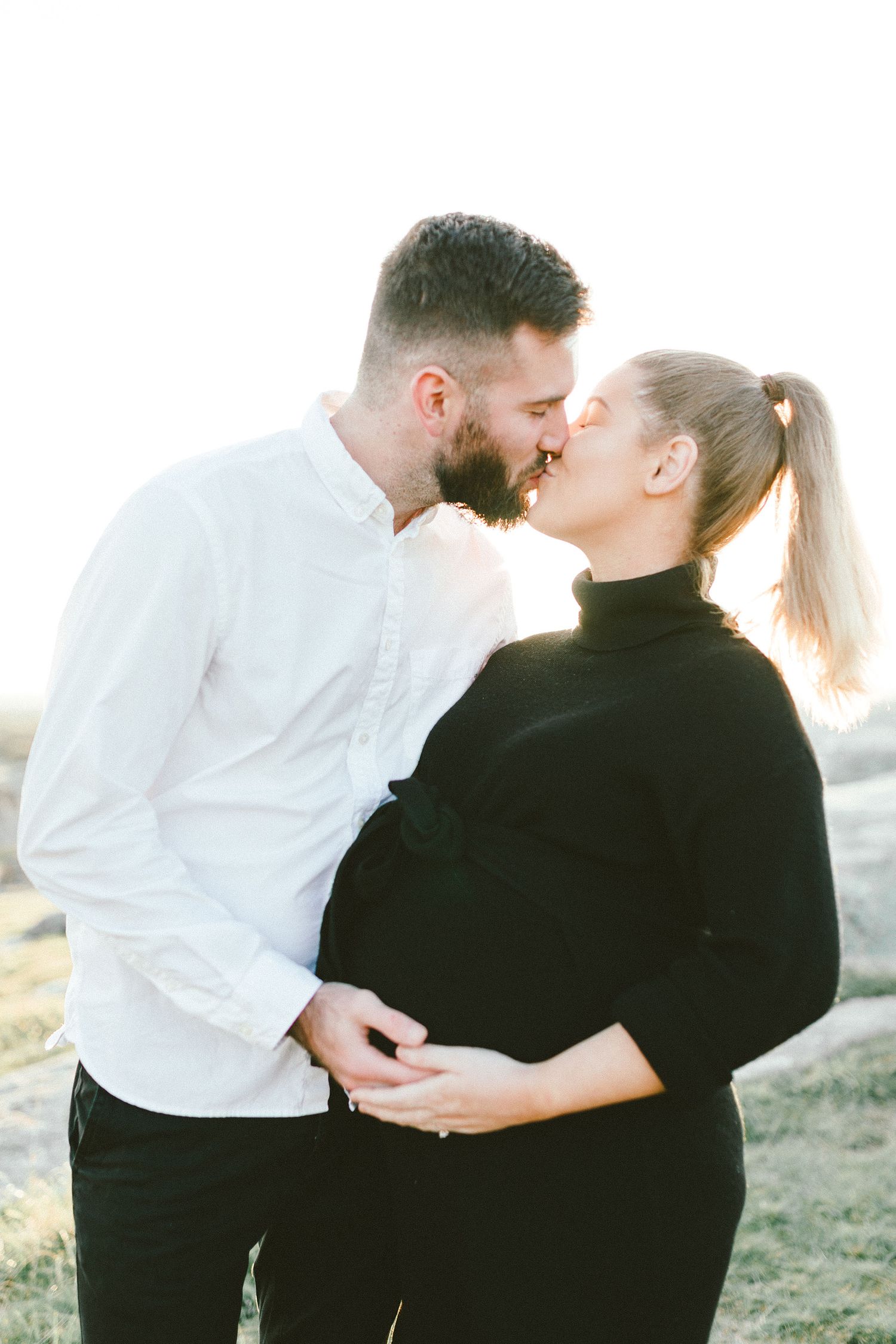 Romantic couple in contrasting outfits share a tender kiss outdoors during a photo session.