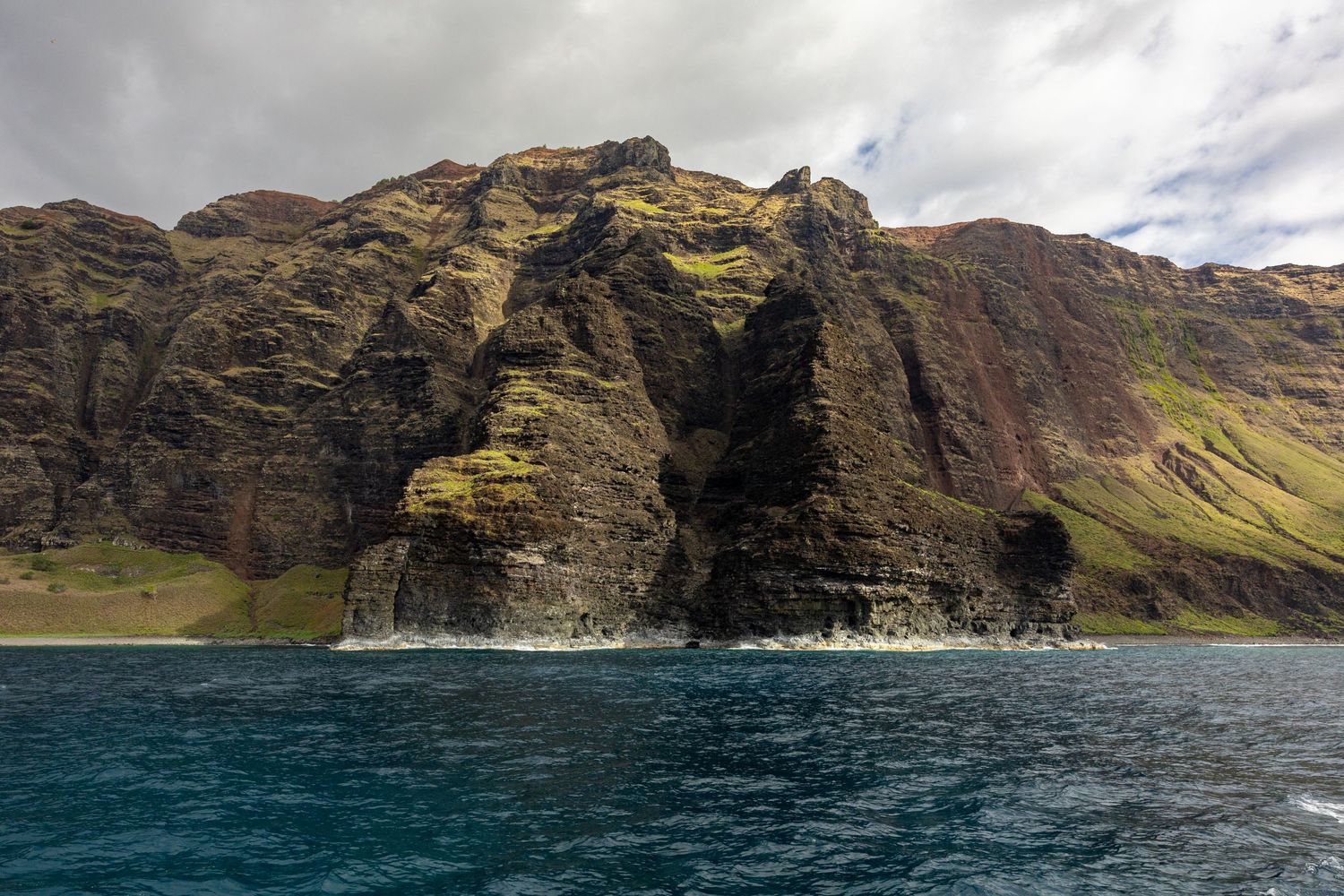 Dramatic coastal cliffs and rock formations rising from turquoise waters under cloudy skies.