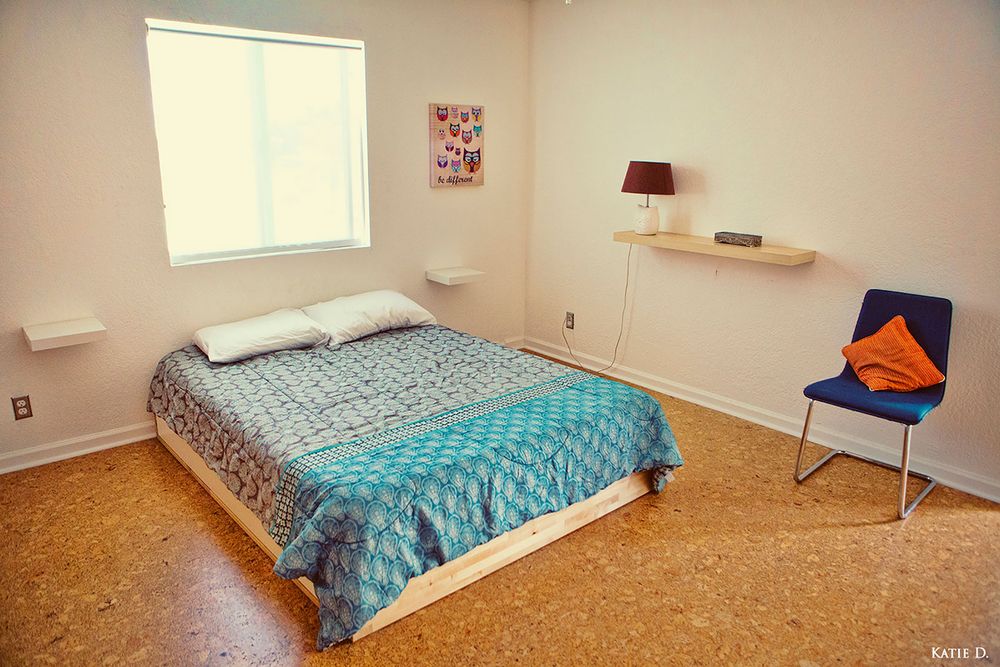 Minimalist bedroom with cork floors, floating shelves, blue bedding, and a modern blue accent chair.