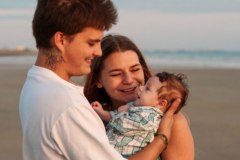 Family embraces on beach during golden hour sunset.