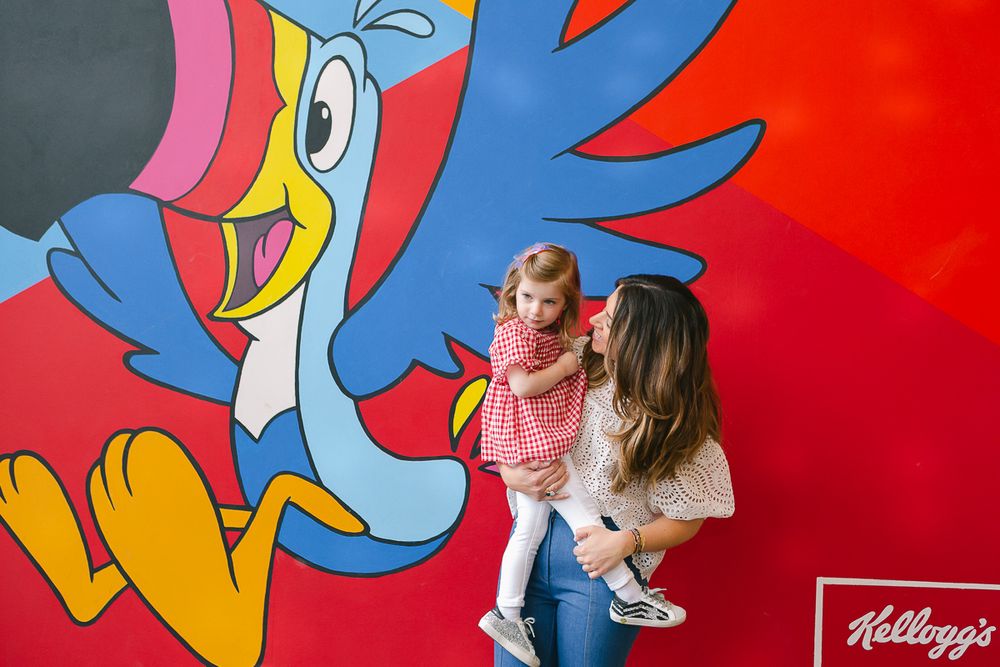 a candid moment of a jewish mother holding her toddler daughter in front of a fruit loops mural at Kellogg's NYC