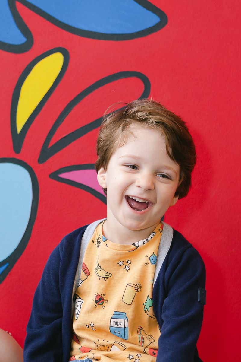 a candid half portrait of a toddler boy laughing against a colorful mural during his birthday party in Manhattan