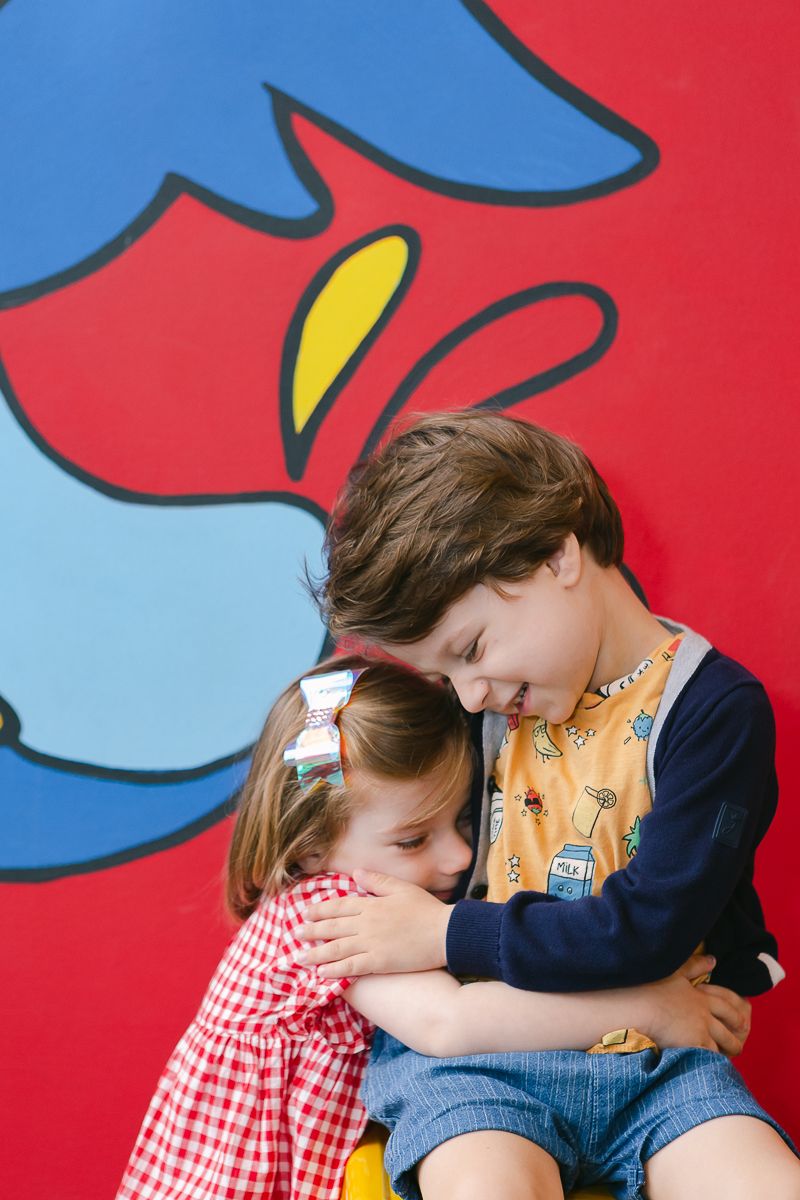 toddler brother and sister hugging against a colorful mural in primary colors photographed by Paula Ortiz NY Family