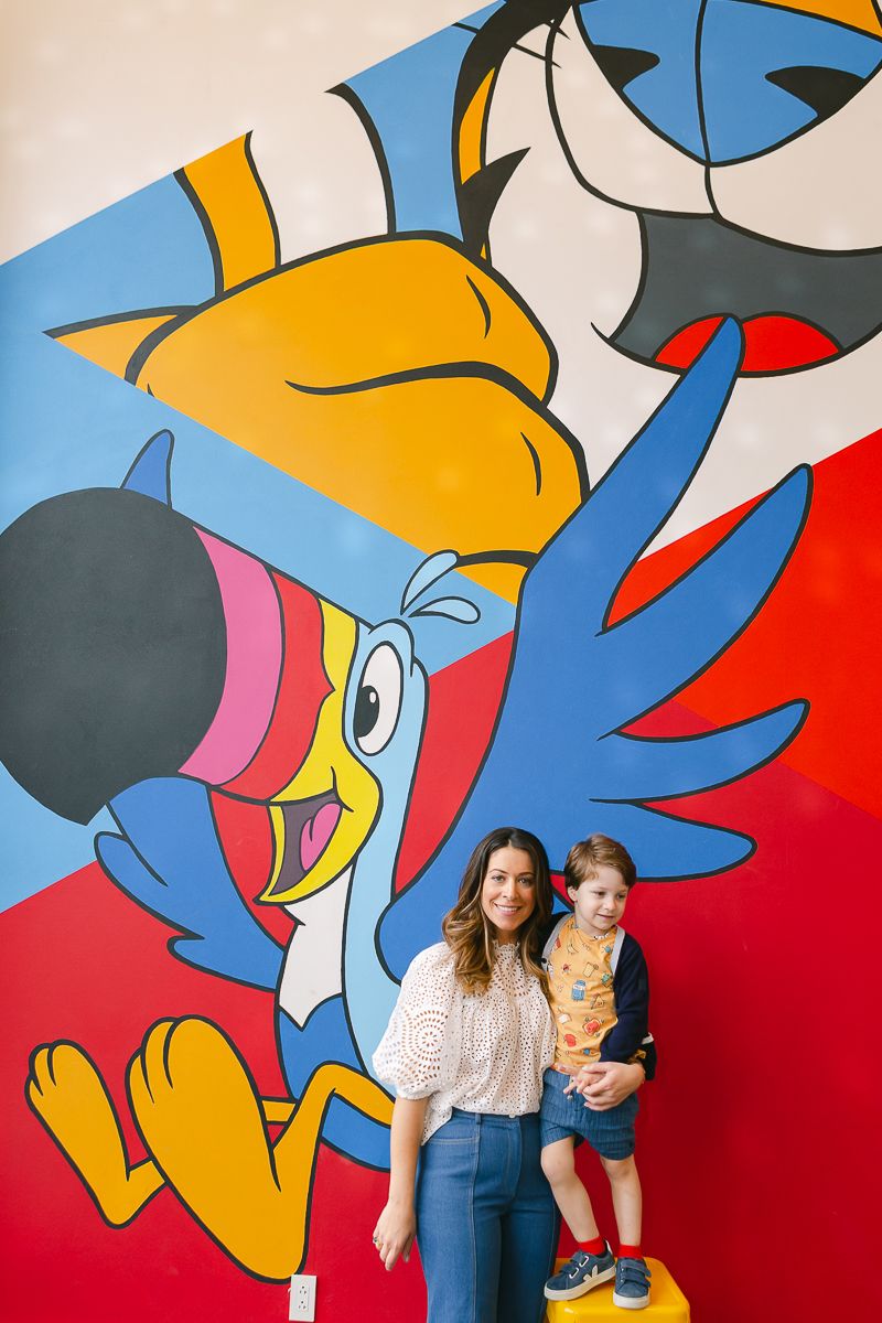 a wide view of a jewish mom and her toddler son standing in front of a a colorful mural of Kelloggs characters in NYC