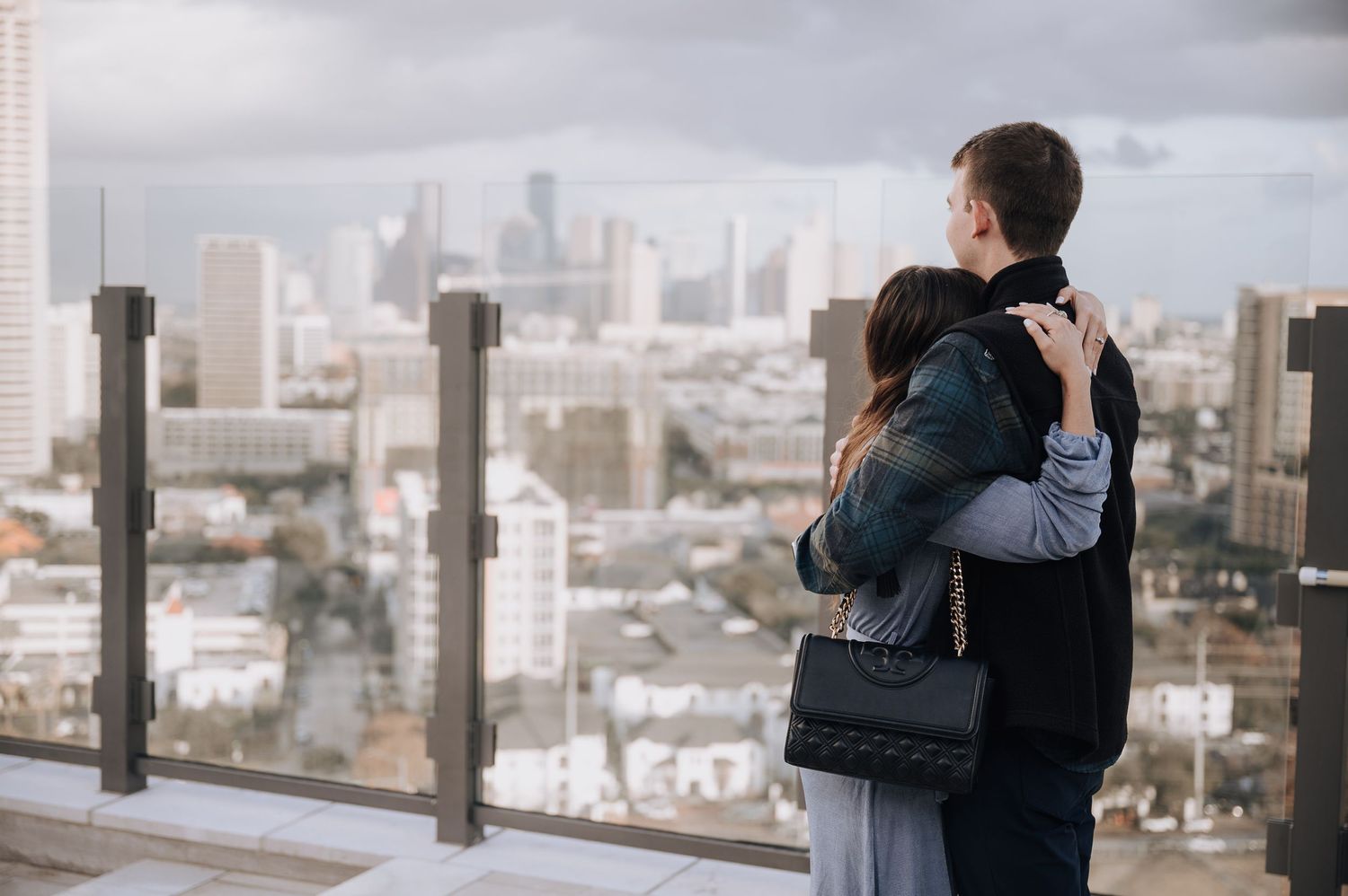 A couple embraces while overlooking a cityscape view from a high observation deck.