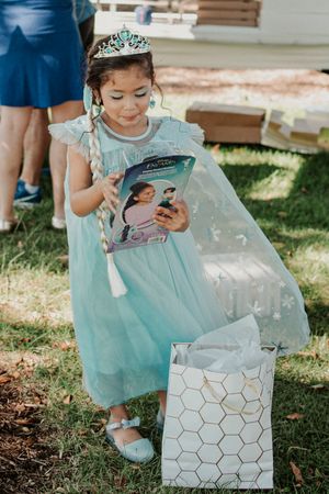 A child in a turquoise dress examines a decorated gift box outdoors.