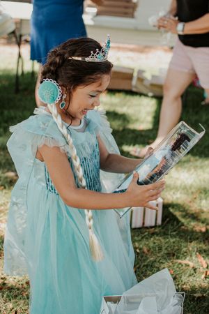 A young party guest in a blue dress explores contents of decorative boxes.