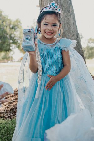 A young attendee in a sparkly blue dress poses with presents at an outdoor celebration.