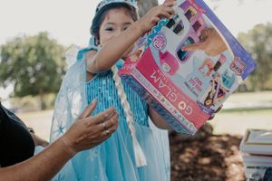 A child holds colorful gift boxes while wearing a festive blue princess dress.