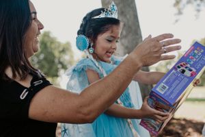 A person in a blue dress excitedly opens presents at an outdoor party.