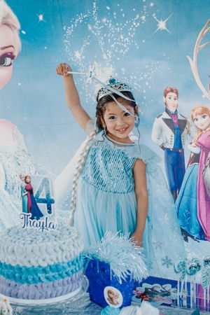 Frozen themed birthday celebration with cake, decorations and sparkly blue backdrop.