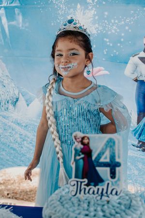 Child in a sparkly blue princess dress celebrating at a Frozen-themed birthday party.