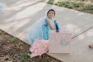 Child in blue dress holding gift box outdoors on concrete path.