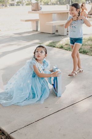 Two children in blue outfits playing on concrete pathway outdoors.