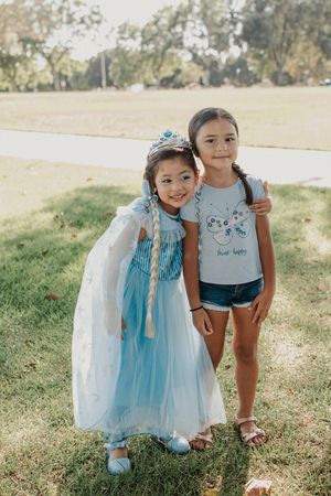 Two children posing together outdoors, one wearing blue princess dress.
