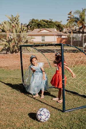 Children playing by soccer goal with ball on grass field.