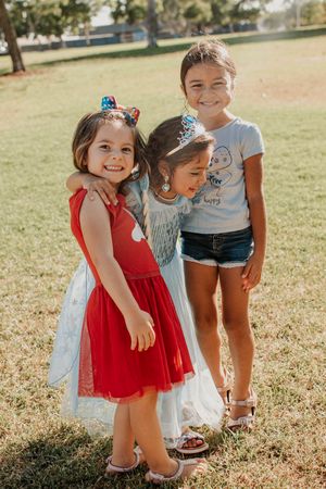 Three children in casual summer attire laughing together outdoors.