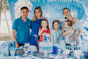 Family gathers around a blue and white birthday cake at a Frozen-themed party celebration.