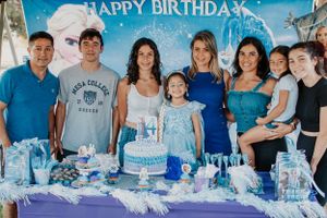 Group photo of party guests around a blue and white birthday cake with Frozen decorations.