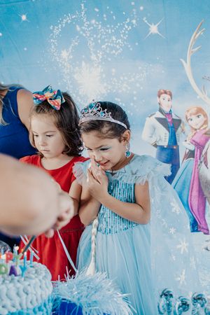 Children gathered around a birthday cake at a Frozen-themed party with decorative backdrop.