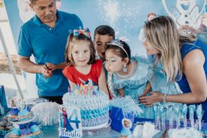 Family members watching as birthday candles are lit on a blue tiered cake at Frozen themed party.