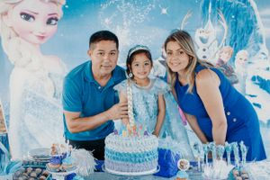 Family poses with blue tiered birthday cake against Frozen movie themed backdrop.