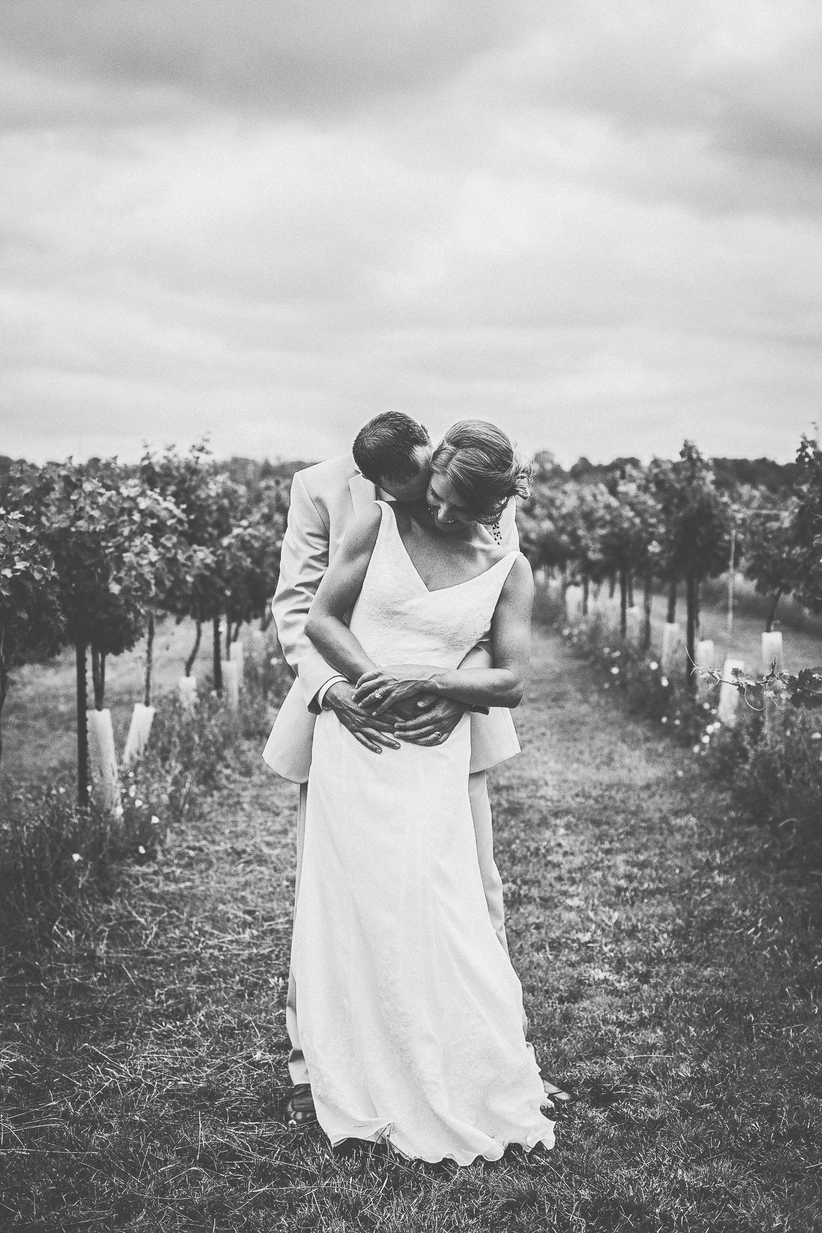 wedding couple bride groom hugging from behind in middle of vineyard