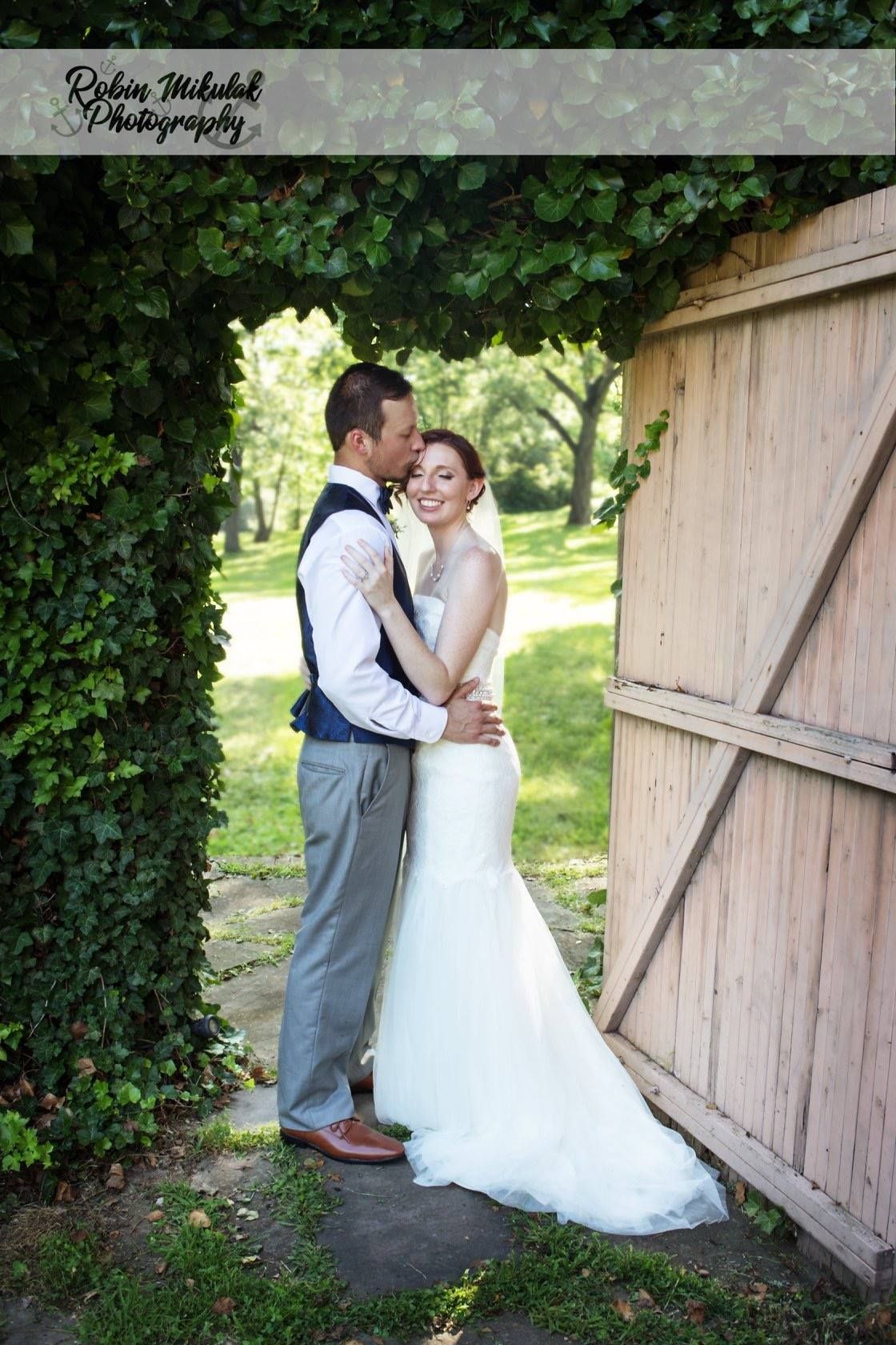 Newlyweds in wedding attire share romantic moments by a rustic wooden barn door.