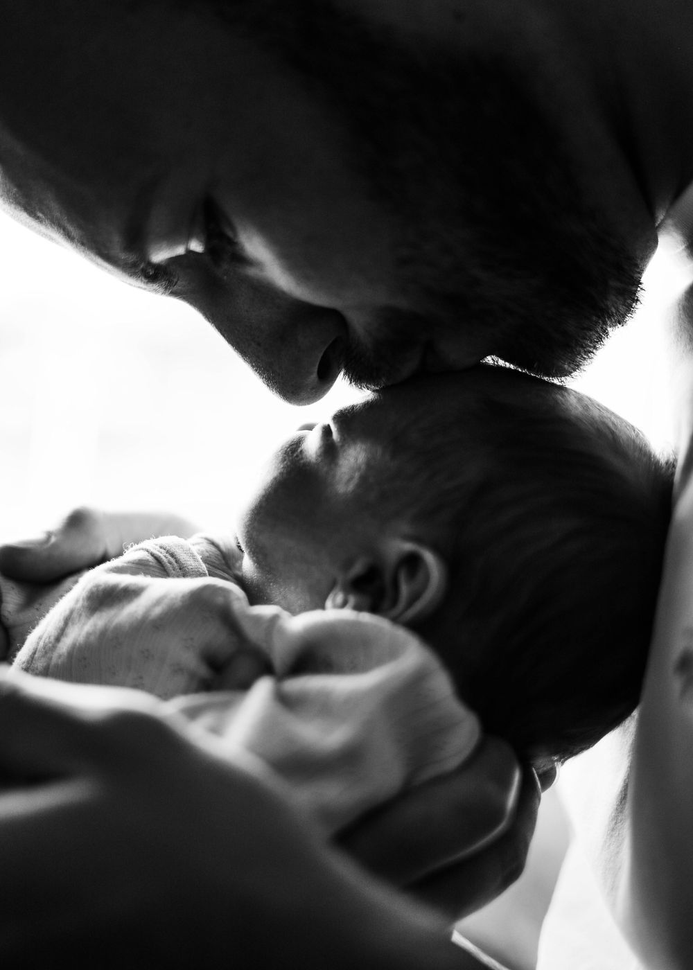 Intimate black and white close-up of tender moment between parent and newborn.