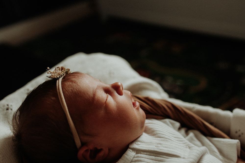 A sleeping baby lies peacefully on white bedding wearing a delicate headband.