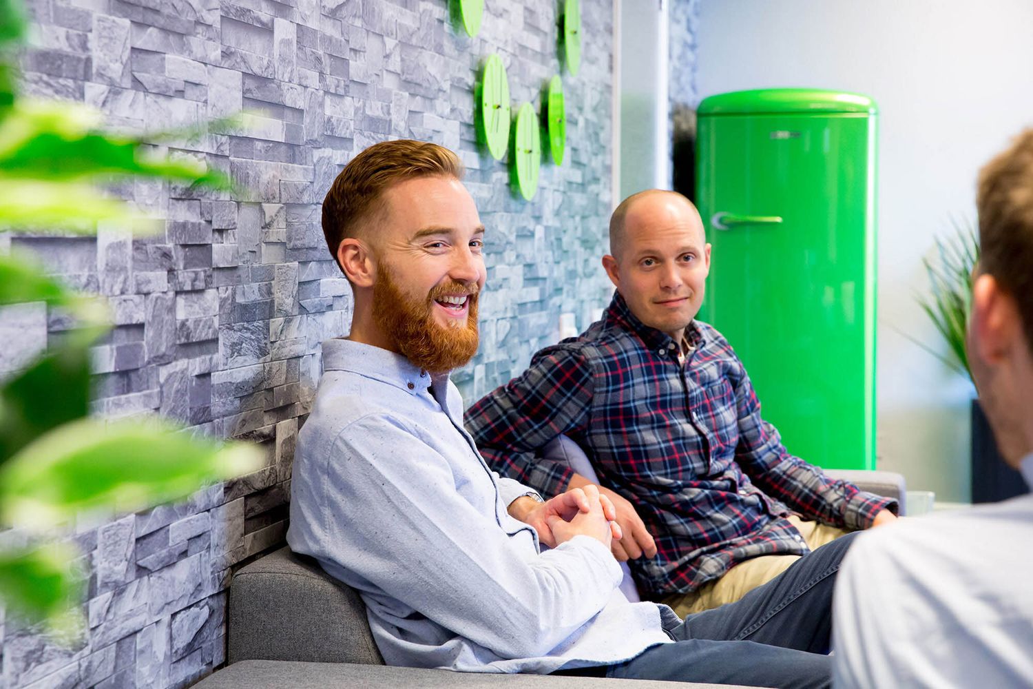 Casual office meeting with people sitting on comfortable seating against stone wall during business branding photoshoot.