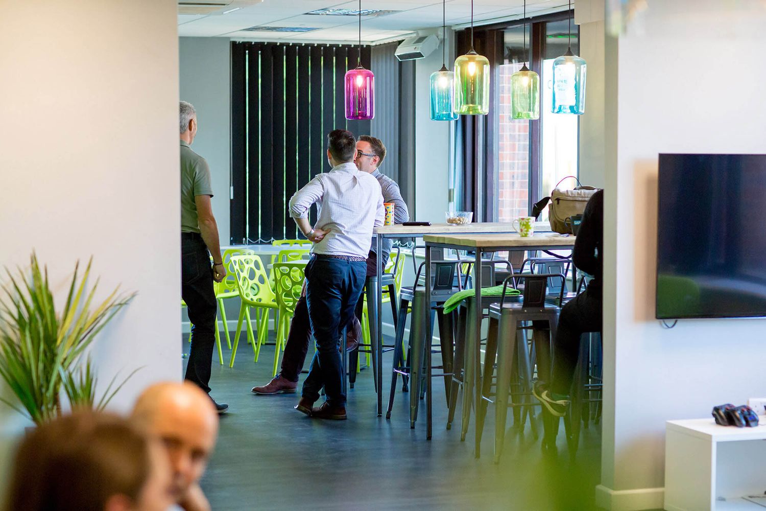 Person standing in modern office space with colorful pendant lights and high tables during business branding photoshoot.