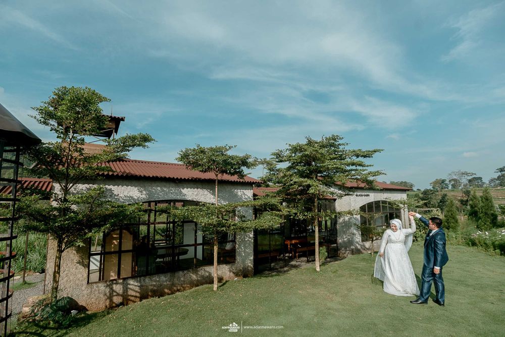 A couple walks along a scenic garden path with buildings and blue sky in the background.