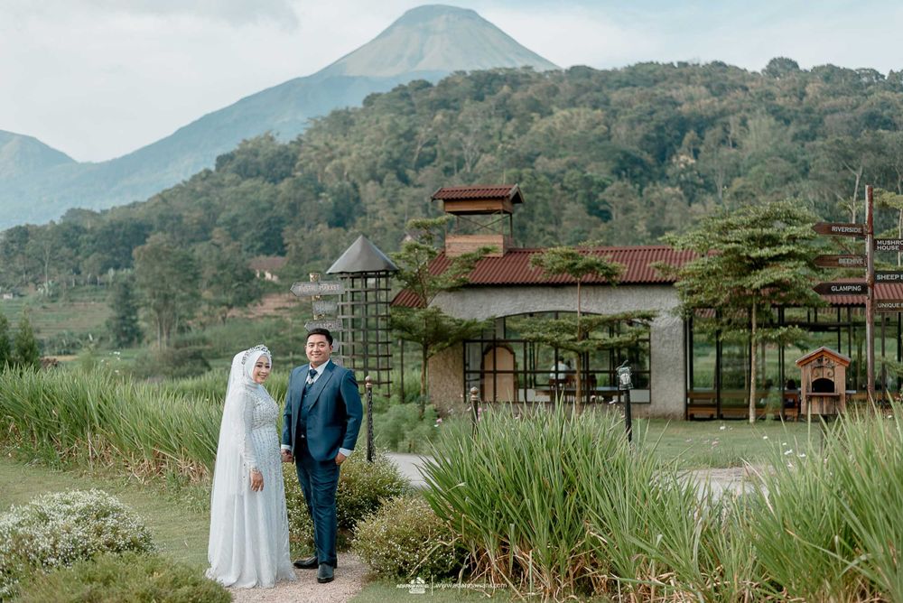 A couple poses in front of a scenic mountain landscape with traditional architecture.