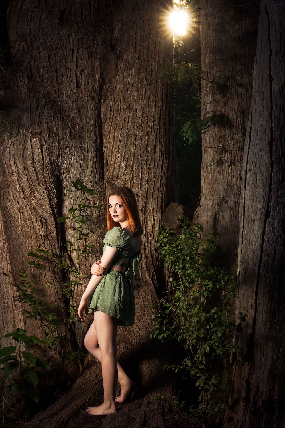 high school senior girl wearing green shorts outfit standing near tall cypress trees with a sunburst at Cibolo Nature