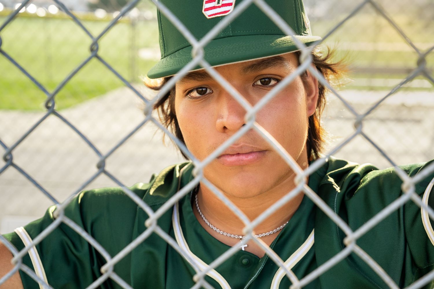 high school senior boy wearing baseball jersey and hat looking through fence of dugout in San Antonio Texas