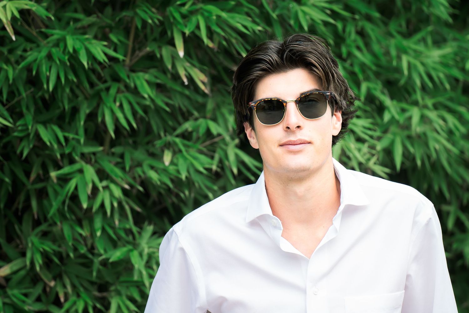 high school senior boy wearing white shirt and sunglasses in front of green bamboo