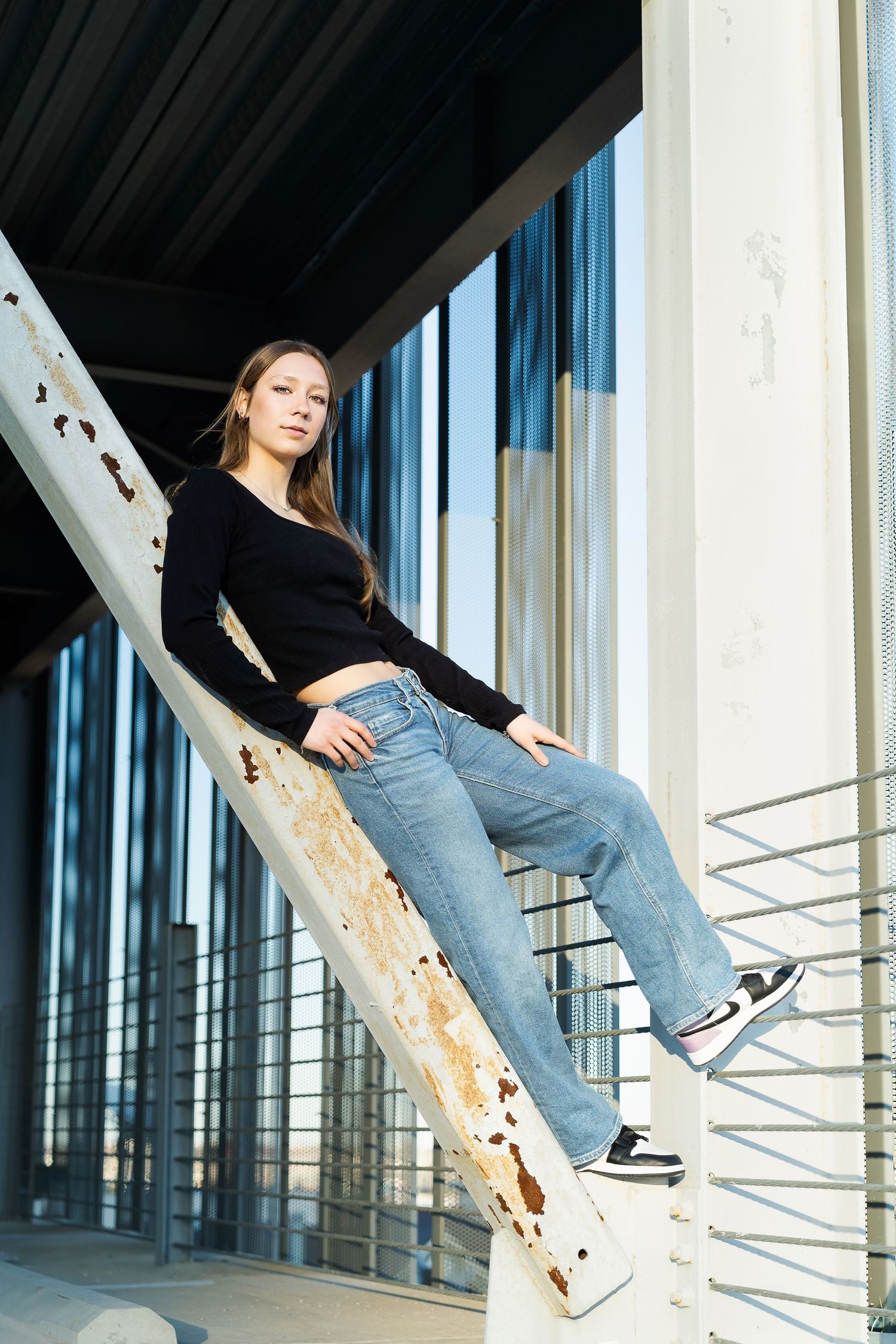 high school senior girl in black sweater and jeans leaning on a beam in a parking garage
