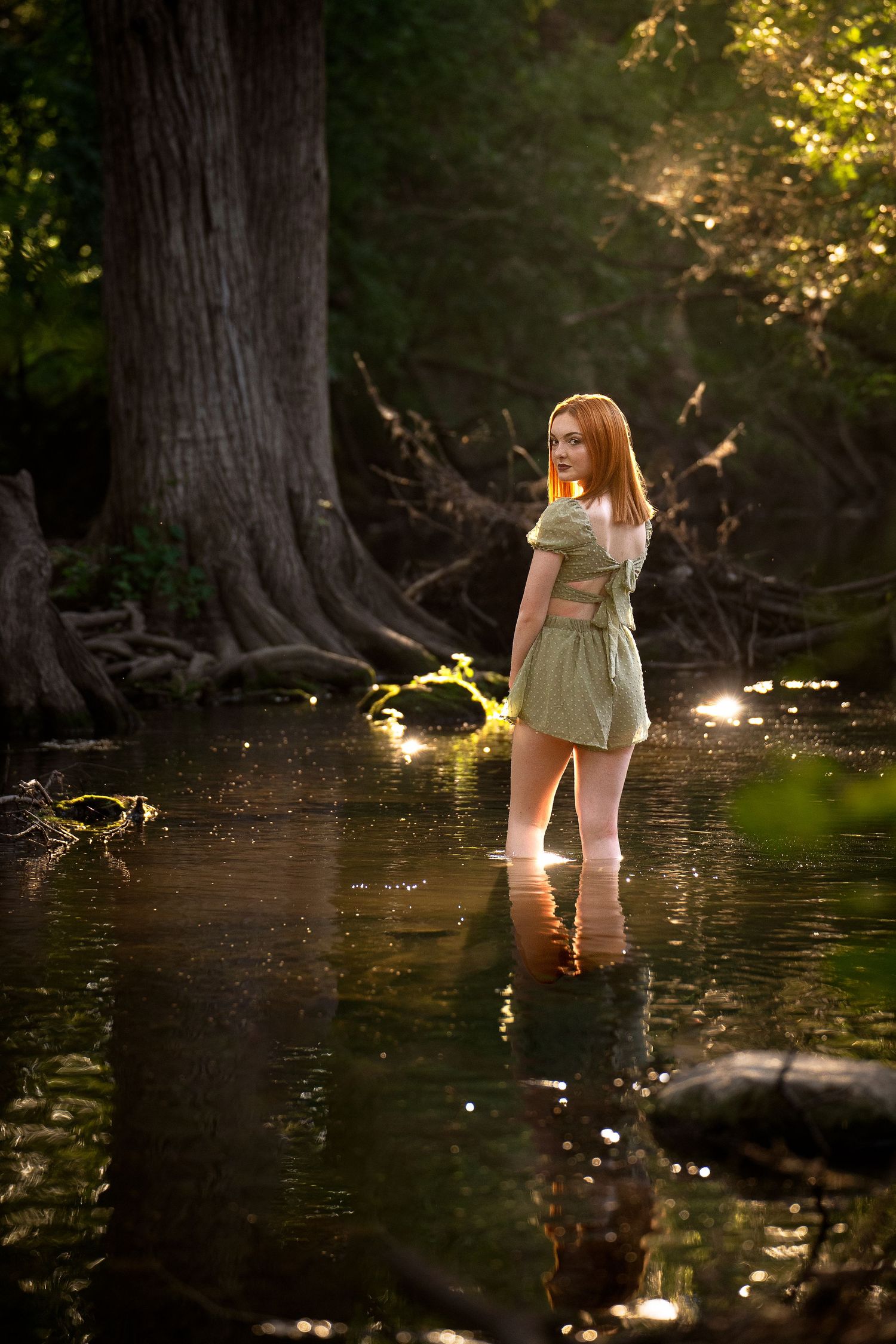 high school senior girl standing in Cibolo Creek wearing green short outfit