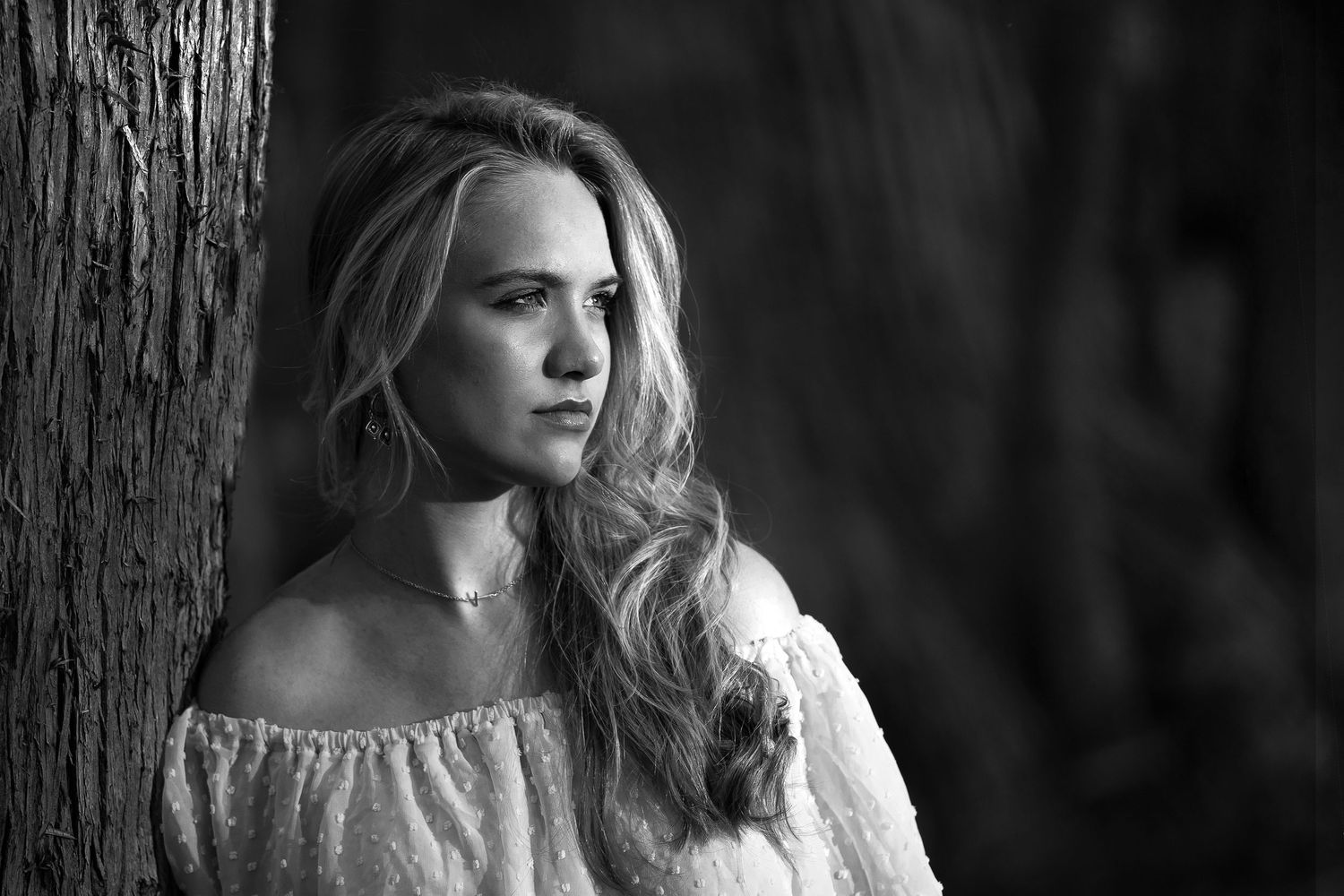 black and white portrait of high school senior girl leaning against a tree looking into the sunlight in Boerne Texas
