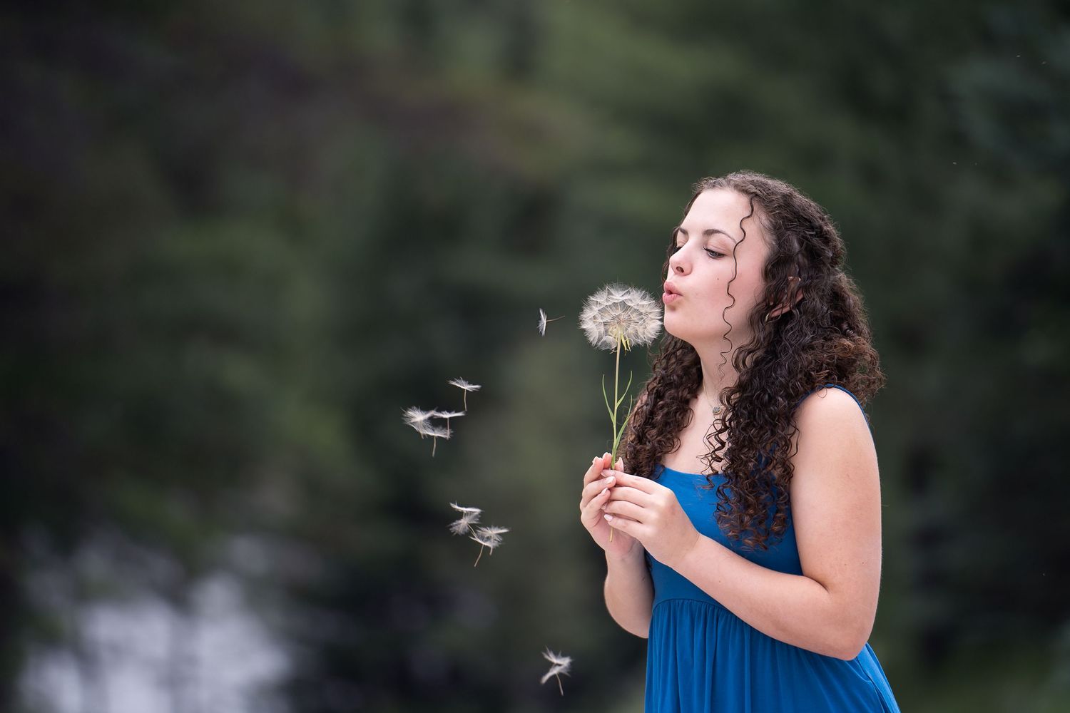 high school girl in blue sundress blowing a dandelion wish flower