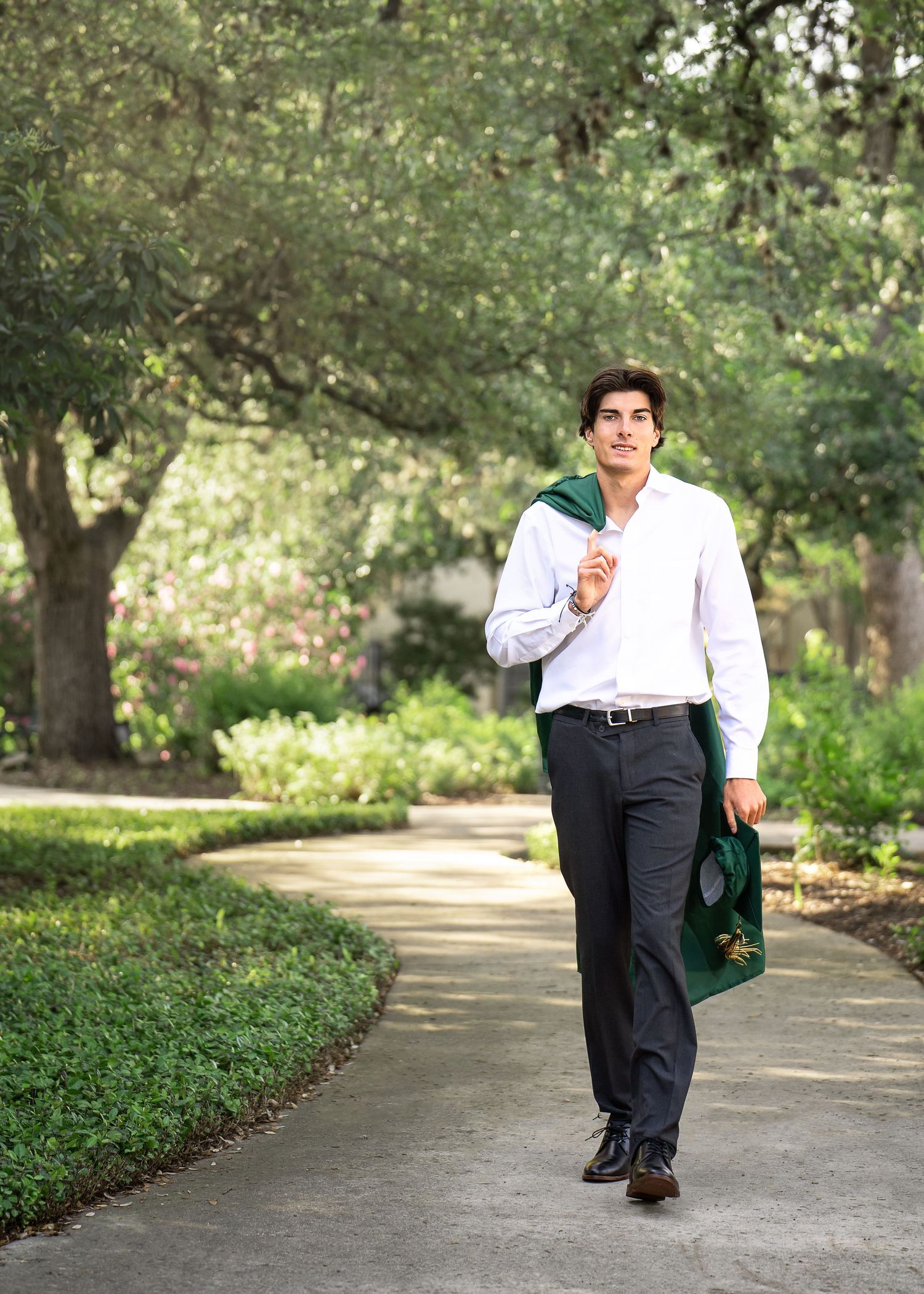 high school senior boy wearing a white shirt carrying cap and gown on walkway at Landa Library
