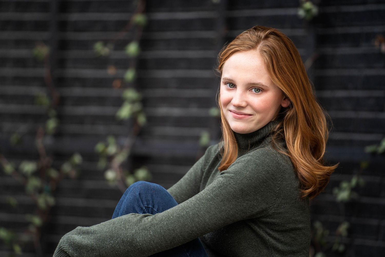 high school senior girl wearing green sweater in front of black wall with green ivy