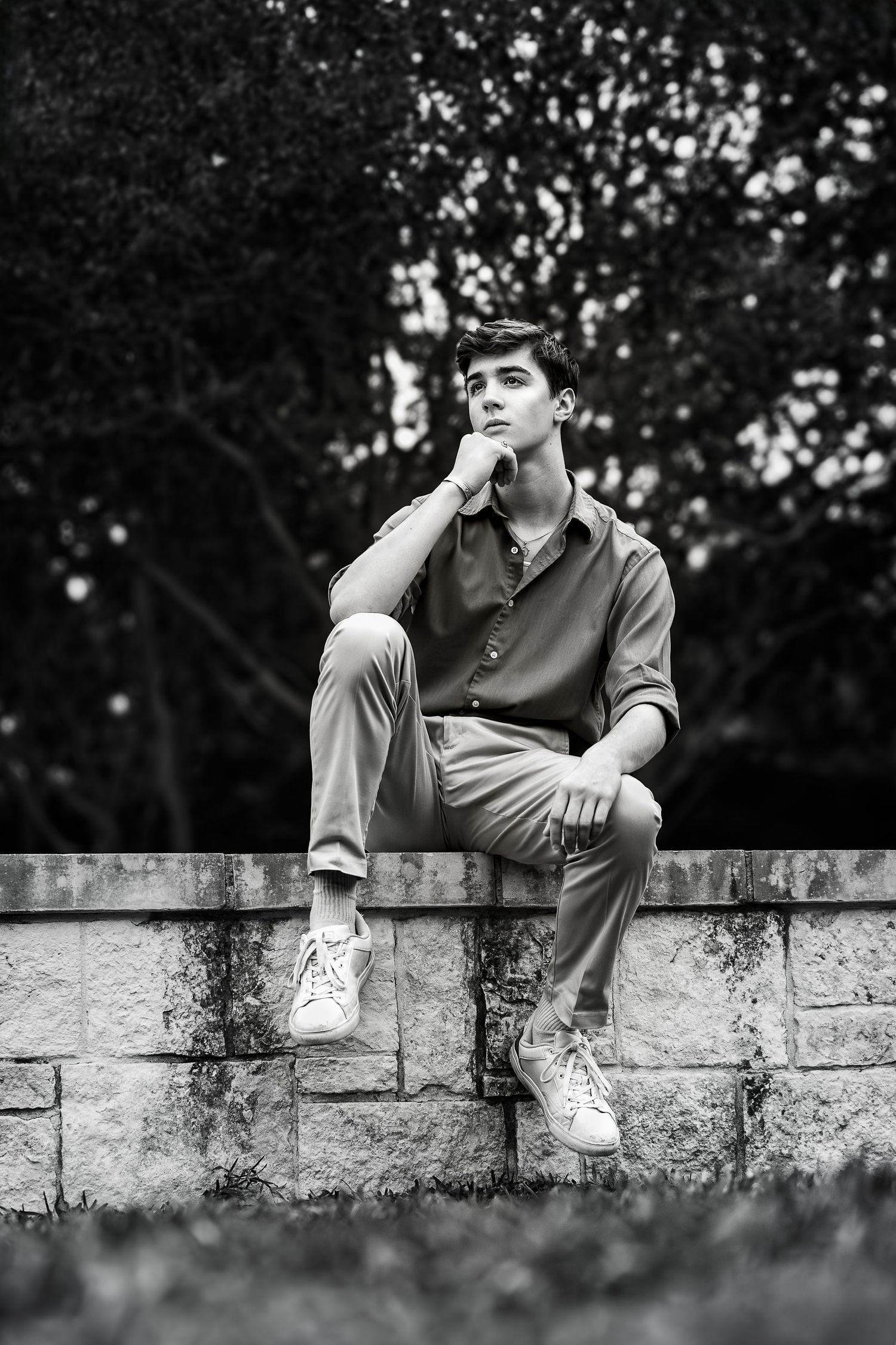 black and white portrait of high school senior boy sitting on a wall in Landa Garden at Landa Library in San Antonio TX