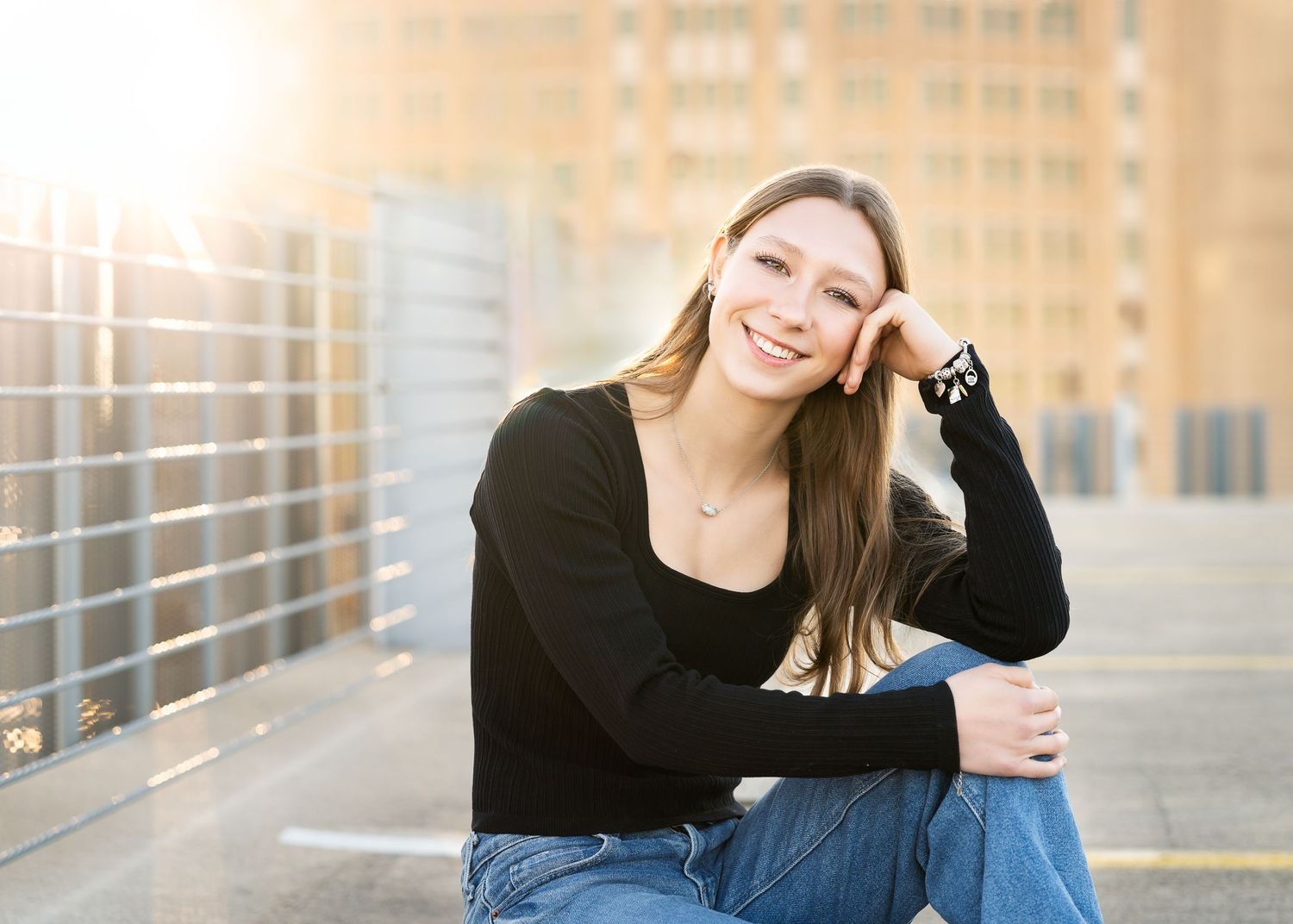 high school senior girl wearing black sweater sitting onto of parking garage with sunburst behind her
