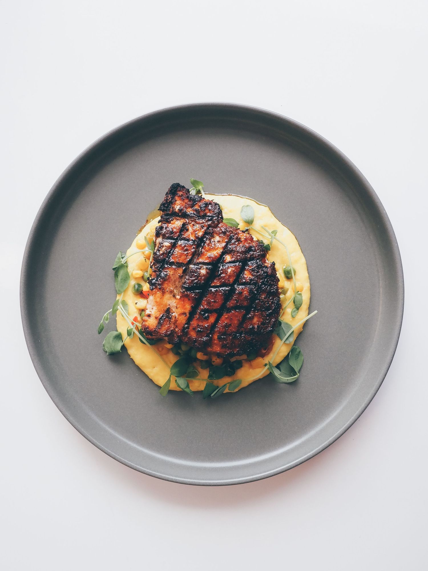 Grilled chicken breast served on a gray plate with creamy sauce and herbs.