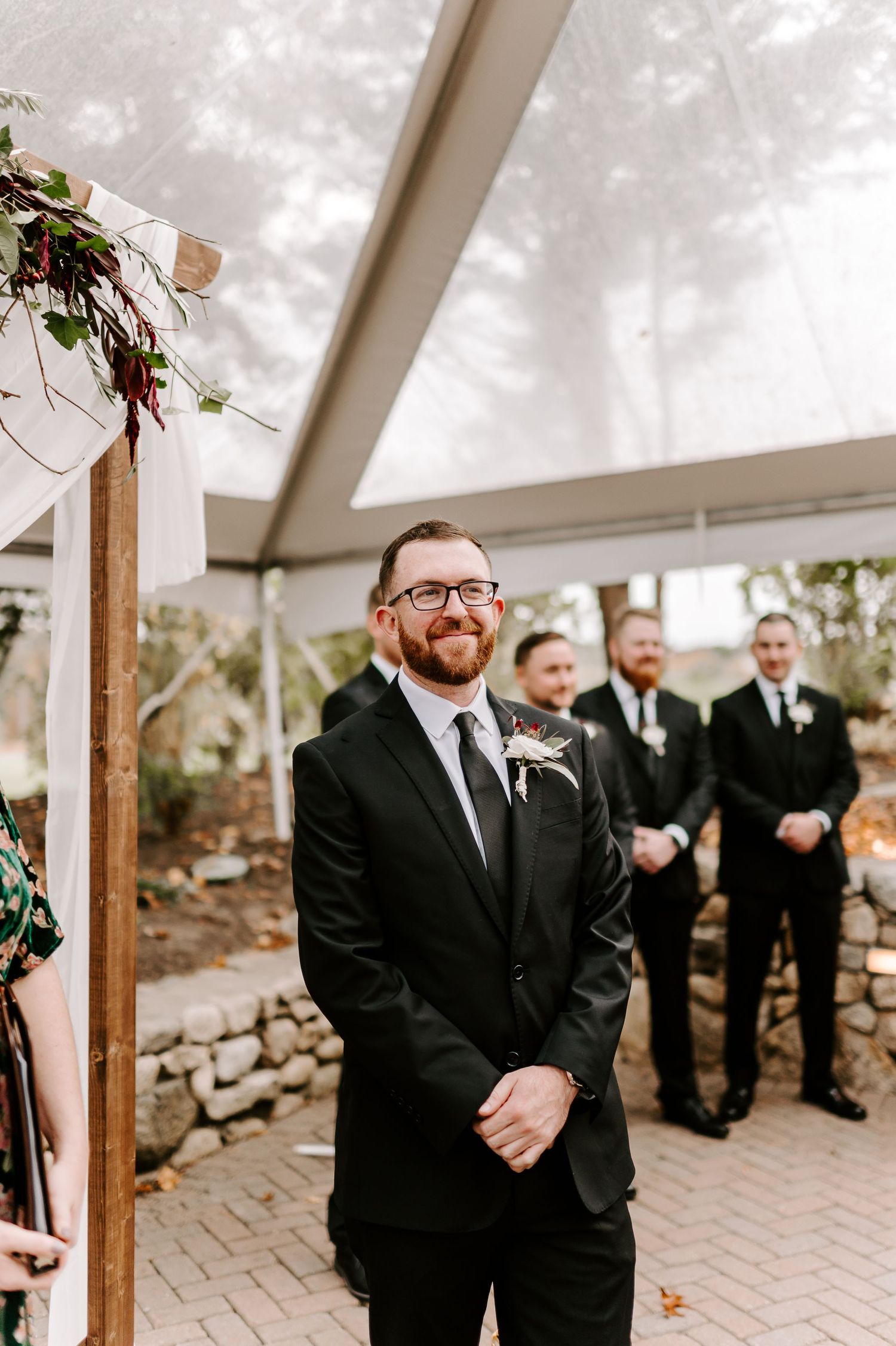 Wedding ceremony setup under a clear tent with guests gathered on a brick patio.