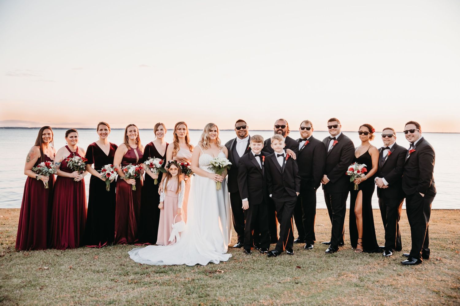 Large wedding party portrait at sunset with bridesmaids in burgundy and groomsmen in black.